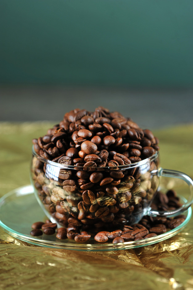 Coffee beans in transparent glass cup on gold Photo.