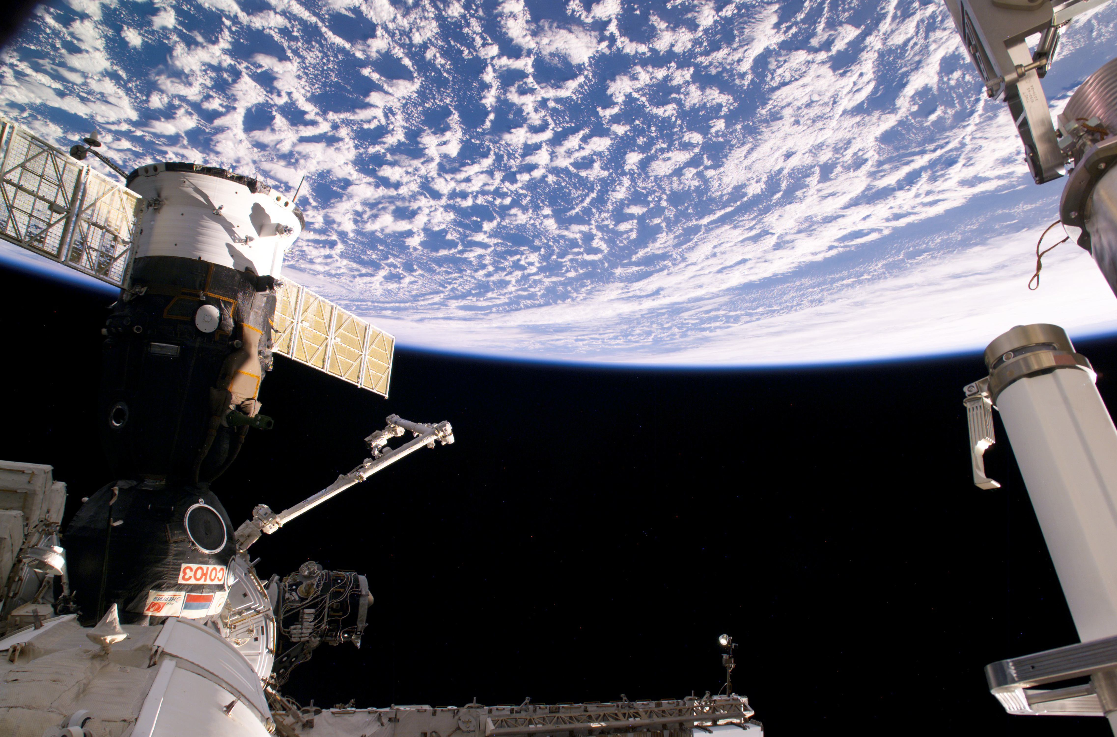 Photograph of A Soyuz Spacecraft and the Canadarm2 With Earth in.